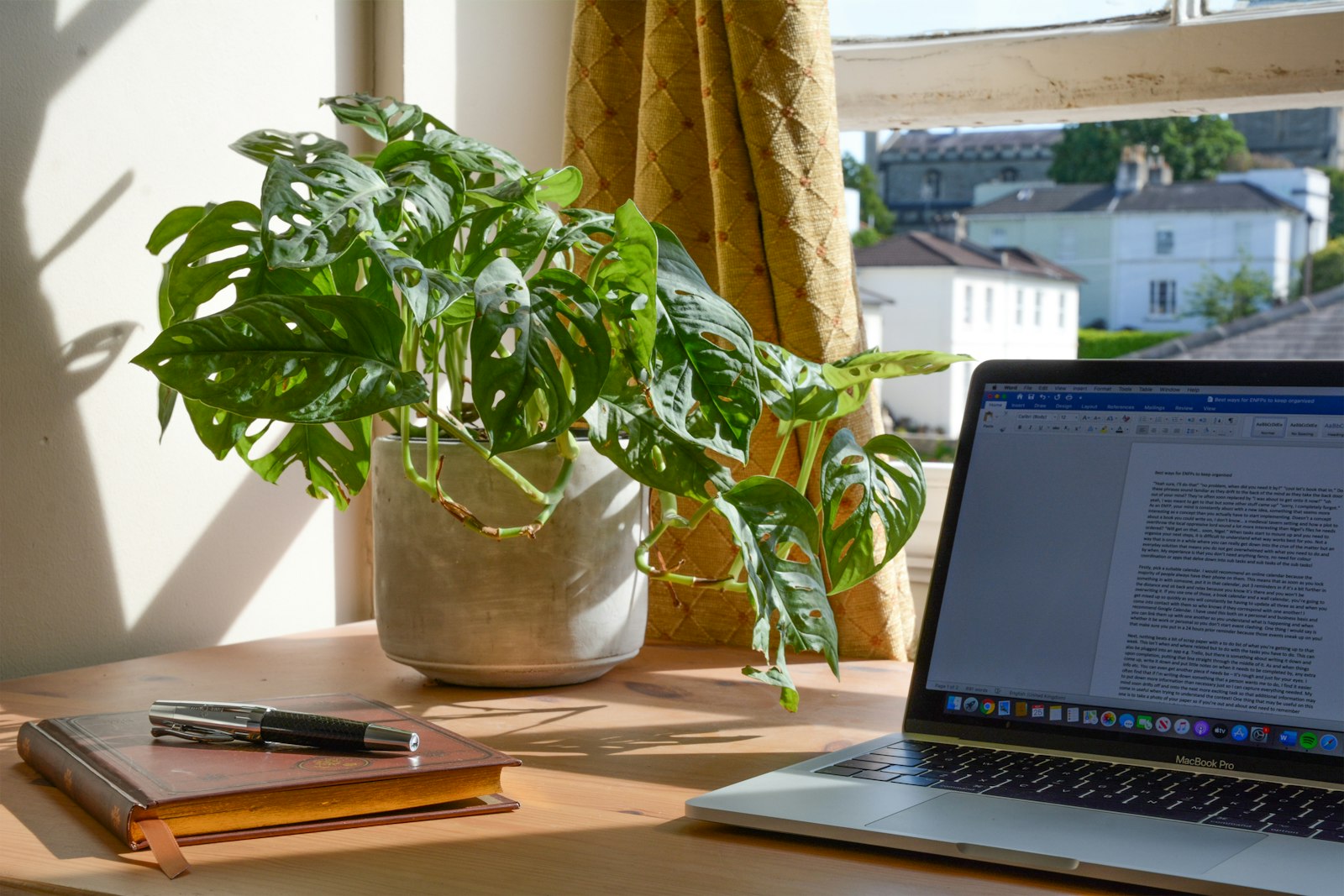 Escritorio con ordenador portátil, cuaderno y una planta junto a la ventana