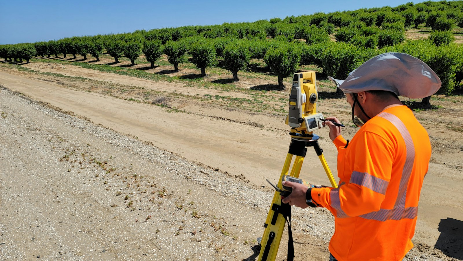 Estación topográfica tomando datos en un camino rural junto a una plantación